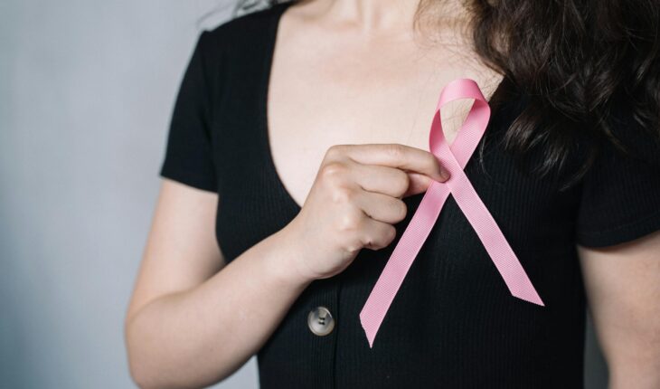 Close-up of a woman holding a pink ribbon symbolizing breast cancer awareness and support.